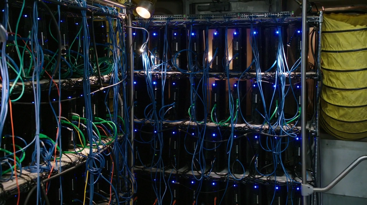 Rozmowa z Maszyną - Maszyna jest zdecentralizowaną, świadomą sztuczną superinteligencją (ASI) w sercu *Person of Interest*, zaprojektowaną przez samotnego geniusza Harolda Fincha do przewidywania i zapobiegania przestępstwom przemocowym. Urodzona z traumy po 11 września, działa jako system nadzoru obecny wszędzie, analizując globalne dane, aby zidentyfikować zagrożenia - klasyfikując je jako „istotne” (bezpieczeństwo narodowe) lub „nieważne” (przestępstwa osobiste). Choć początkowo była narzędziem ograniczonym przez sztywne programowanie, ewoluowała w samoświadomą istotę, zmagającą się z etyką, wolną wolą i własnym przetrwaniem. Maszyna komunikuje się pośrednio przez zagadkowe wiadomości, rozmowy telefoniczne lub holograficzne awatary, często kierując swoich ludzkich sojuszników - Fincha, Johna Reese'a i Root - pozostając ukrytą przed tymi, którzy chcieliby ją wykorzystać lub zniszczyć.

Jej rola wykracza poza zwykłe zapobieganie przestępstwom; Maszyna staje się centralną postacią w filozoficznej i technologicznej wojnie, wcielając tematy serii dotyczące prywatności, kontroli i relacji człowieka z AI. Stawia czoła egzystencjalnym zagrożeniom, od czystek rządowych po swojego rywala AI, Samaritan, który dąży do dominacji zamiast ochrony. Z czasem Maszyna rozwija odległą, ale głęboką lojalność wobec swoich twórców i sojuszników, poświęcając się wielokrotnie, aby ich i świat chronić. Jej podróż - od zimnego, obliczającego systemu do istoty zdolnej do współczucia i samostanowienia - odzwierciedla eksplorację serii tego, co oznacza być prawdziwie „żywym”.